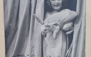 Tyttö pupu kainalossaan kurkkaa verhojen takaa, p. 1905
