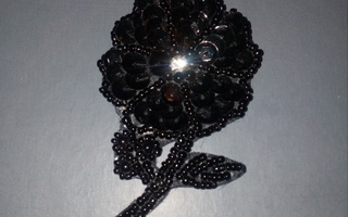 Musta paljetein ja helmin koristeltu kukka